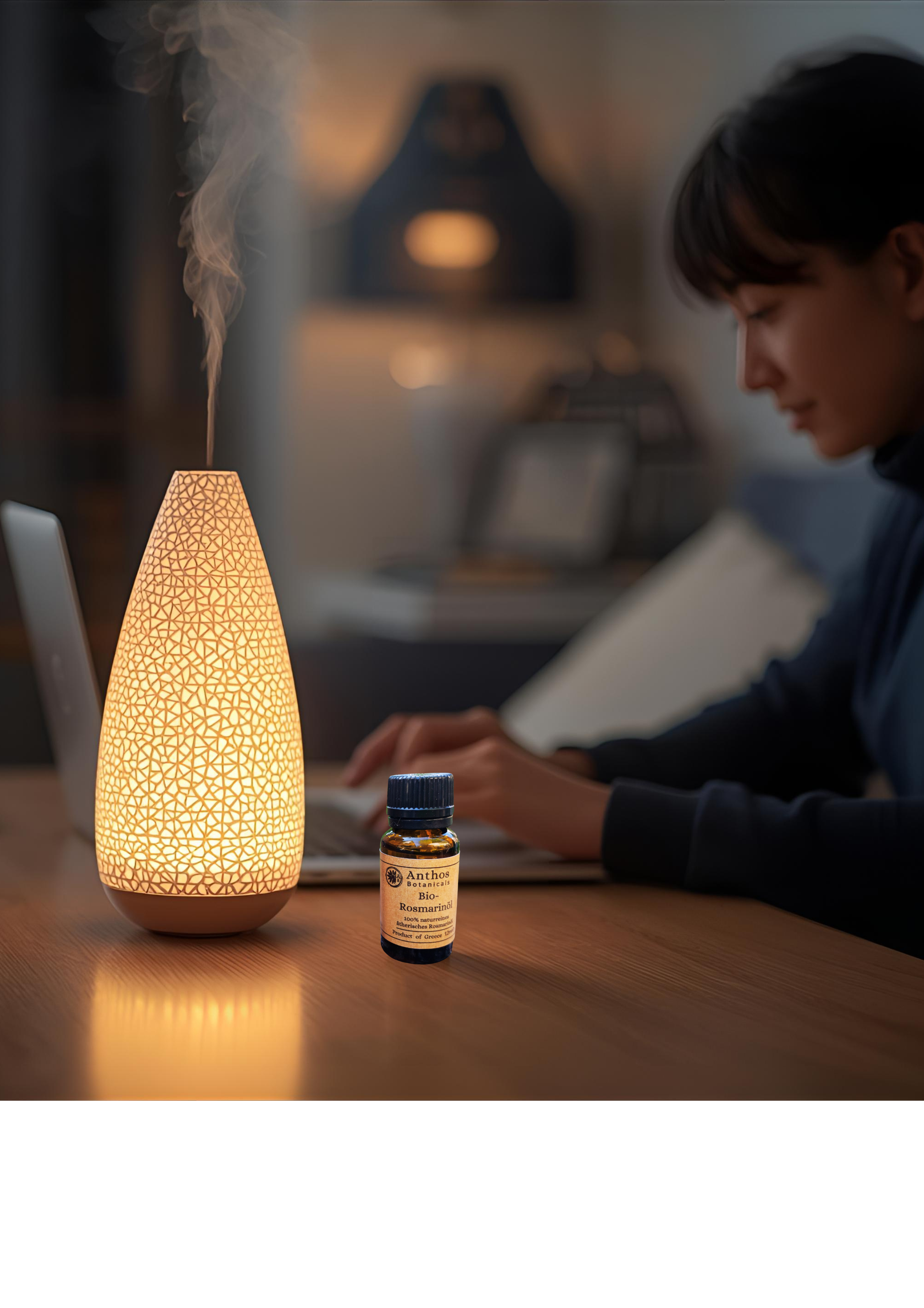 Eine Person arbeitet am Laptop im Homeoffice und hat eine Duftlampe mit Rosmarinöl in Betrieb.