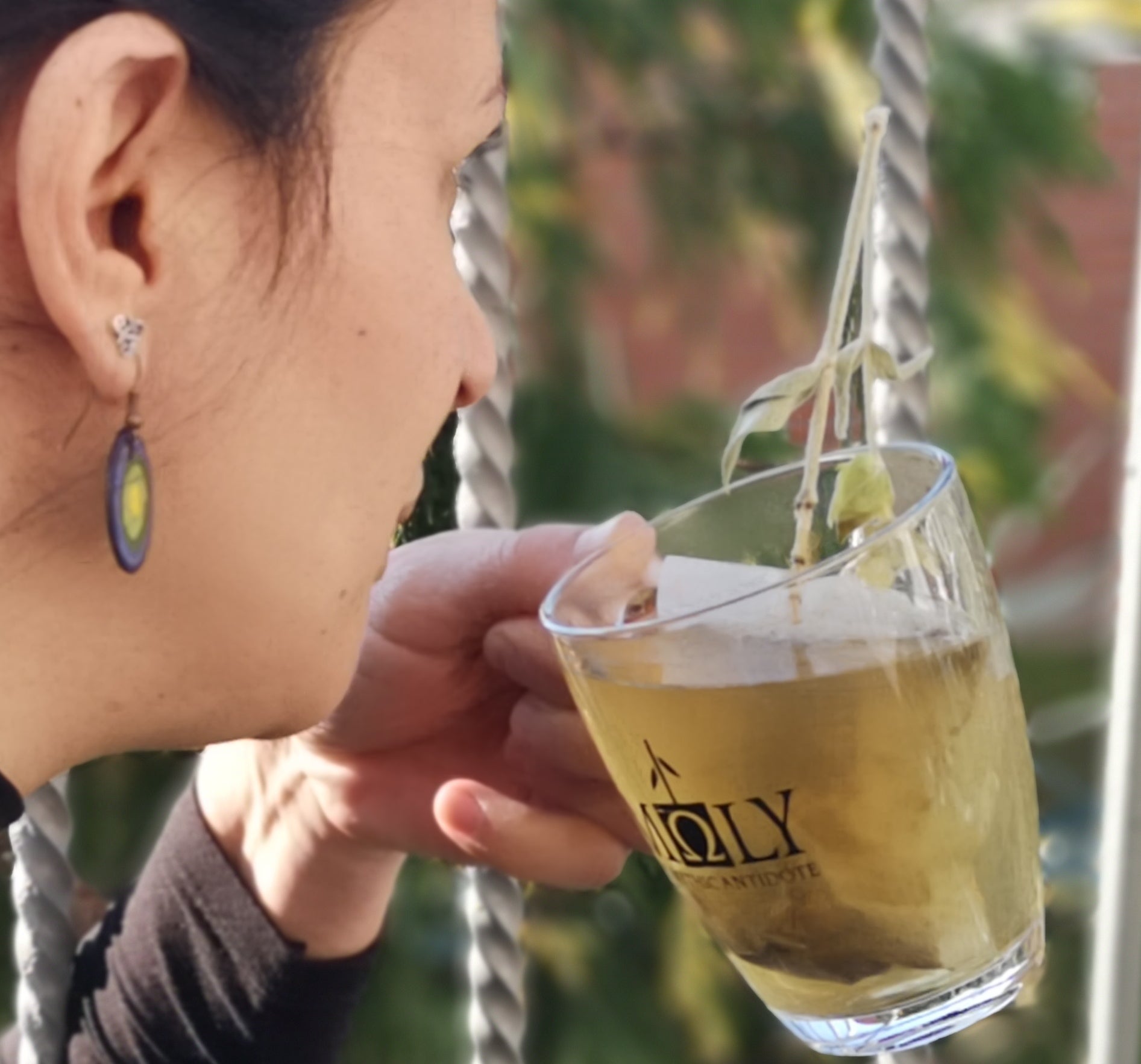 Eine Frau hält ein Glas mit Moly Tee und ist im Begriff einen Schluck Tee zu trinken.