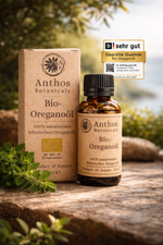 Kraftverpackung und Braunglasflasche mit ätherischem Oreganoöl bio von Anthos Botanicals auf einem Felsen mit Oreganopflanzen in einer mediterranen Landschaft.
