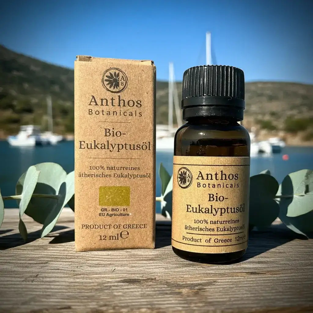 Kraftverpackung und Braunglasflasche mit Eukalyptusöl Bio von Anthos Botanicals vor einem Hafen mit Segelbooten. 