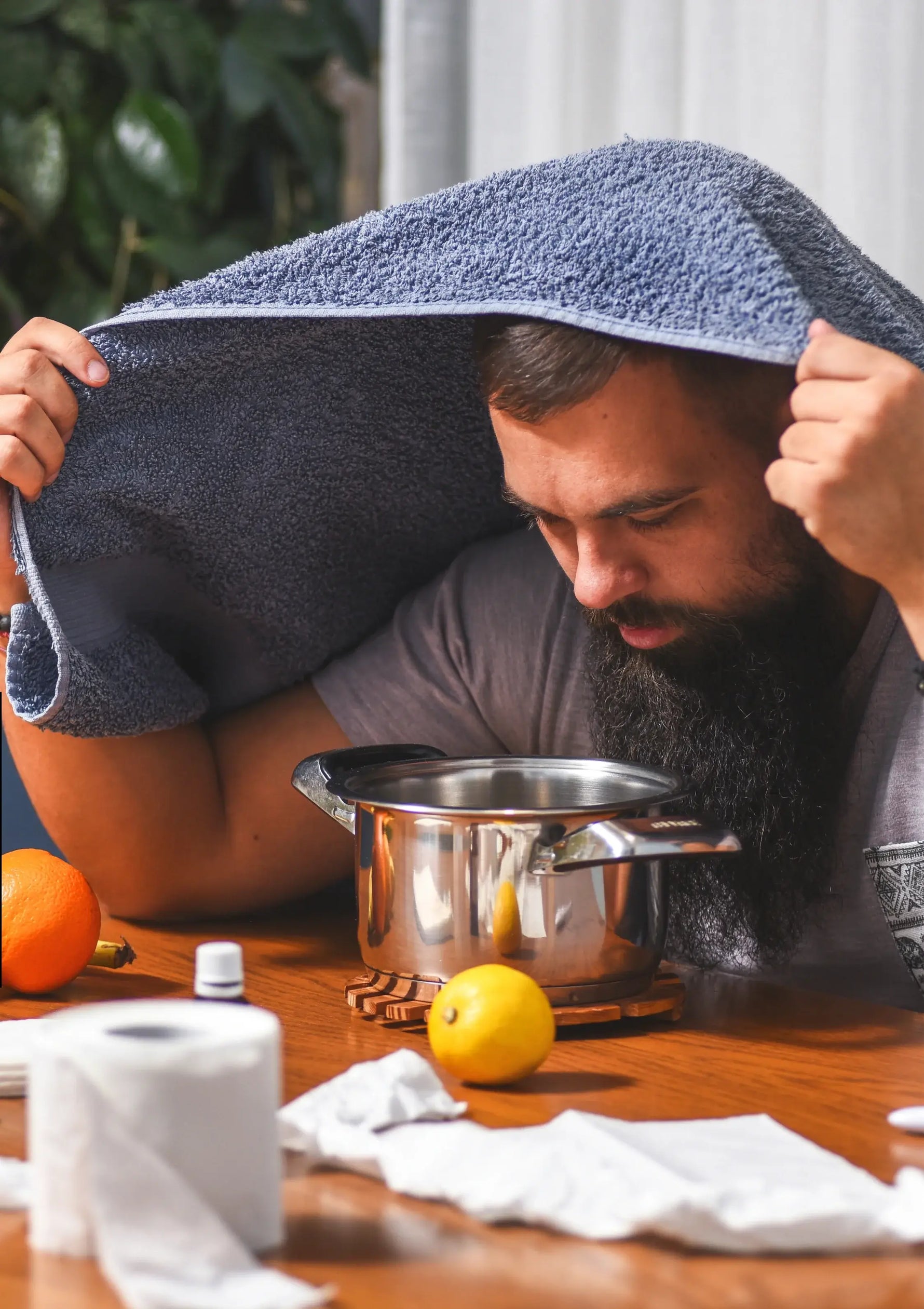 Ein junger Mann sitzt auf einem Stuhl mit einem Handtuch über dem Kopf und inhaliert ätherisches Öl bio von Anthos Botanicals.