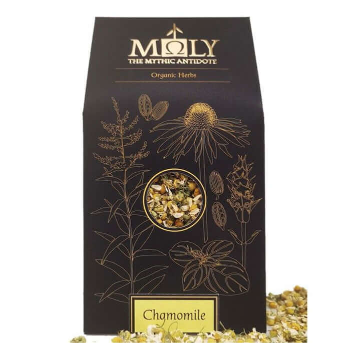 Eine schwarze Verpackung des Kamillenblütentee BIO. Ein Sichtfenster ist vorhanden und man erkennt Kamillenblüten. Kamillenblüten liegen vor und neben der Verpackung.