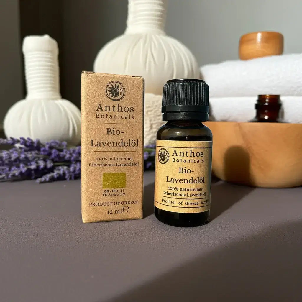 Eine Braunglasflasche mit ätherischem Lavendelöl bio von Anthos Botanicals nebst ihrer Kraftverpackung auf einem Tisch mit Spa-Utensilien