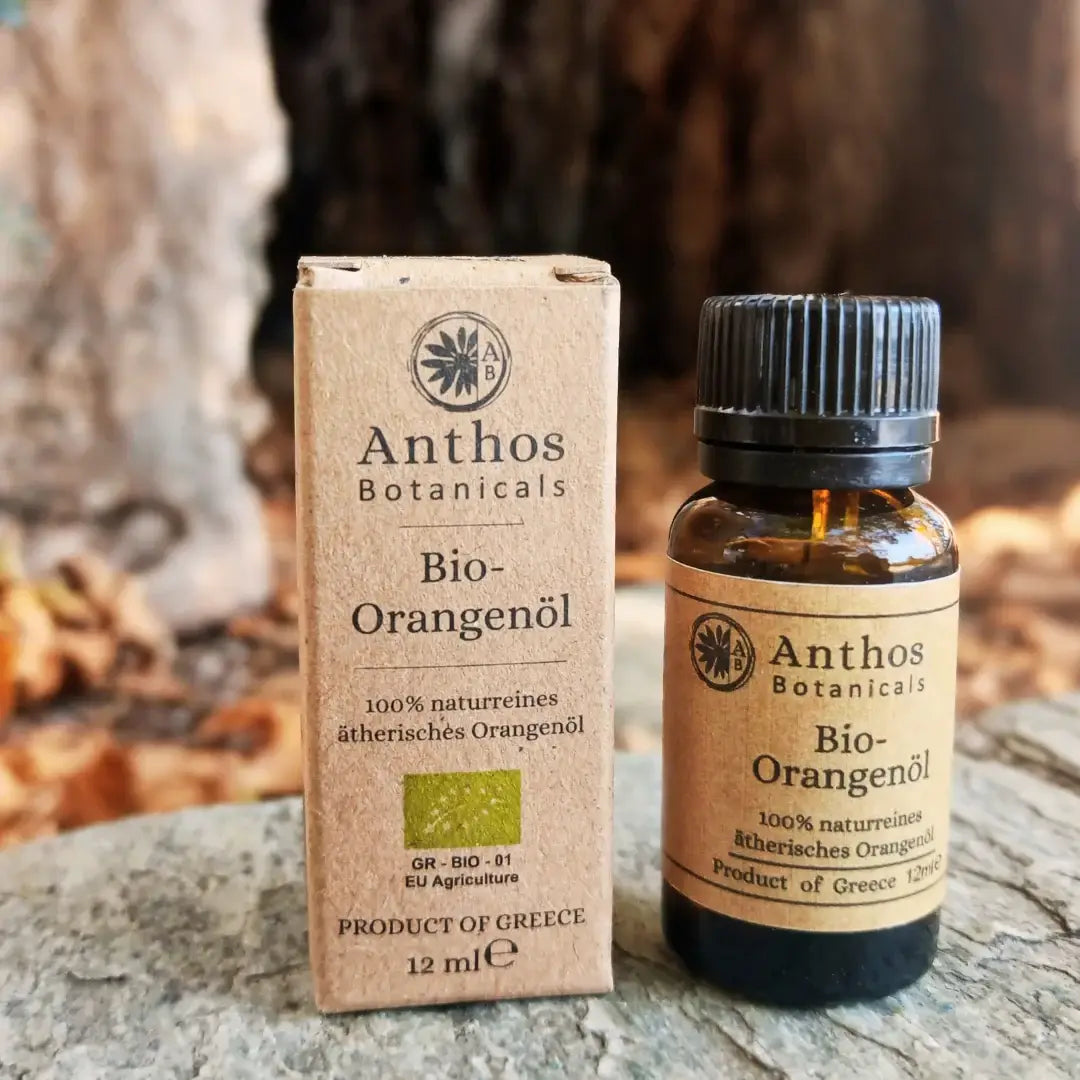 Kraftverpackung und Braunglasflasche mit ätherischem Orangenöl bio von Anthos Botanicals auf einem Felsen in der Natur.