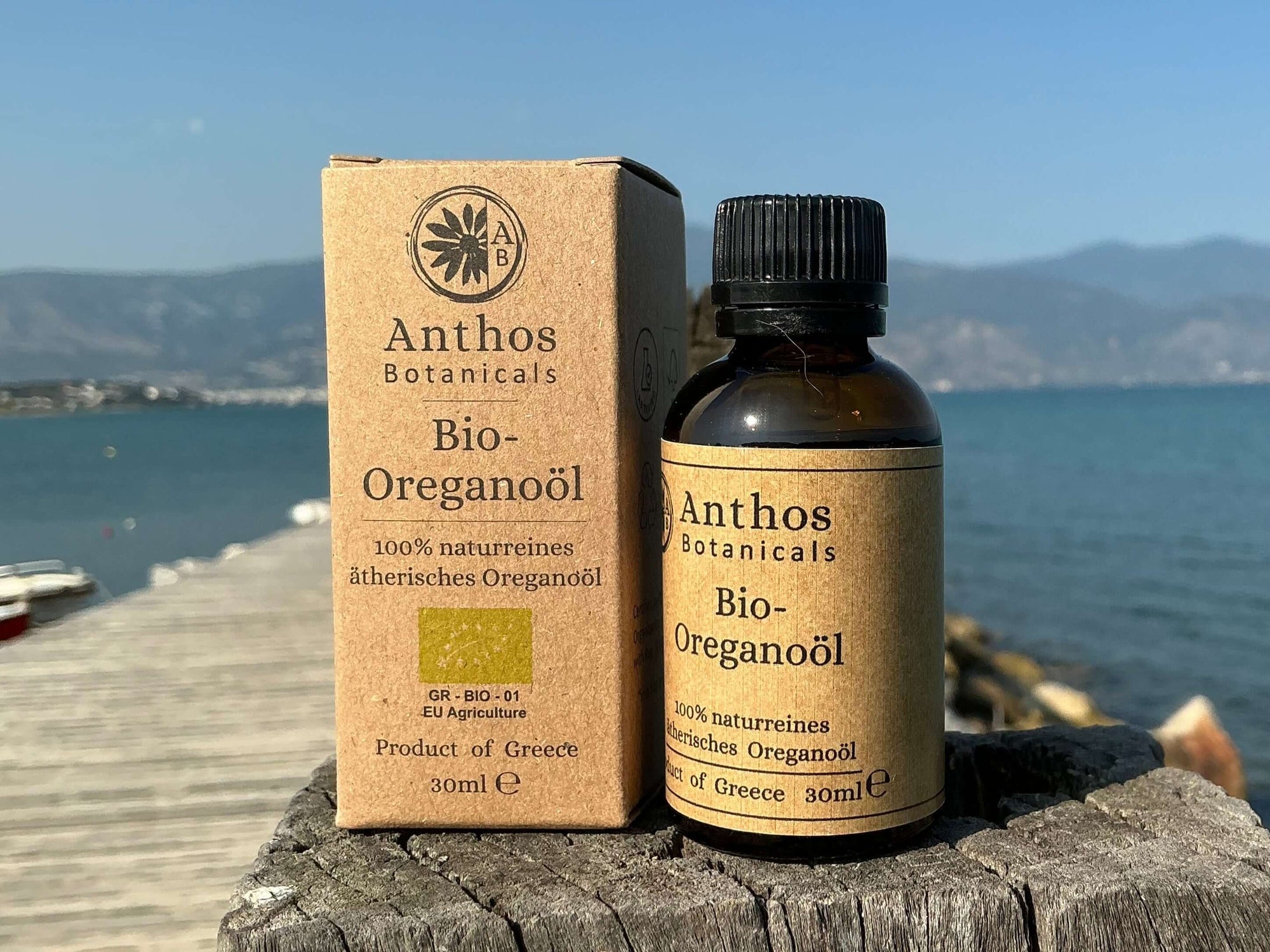 Kraftverpackung und Braunglasflasche mit biologischem Oreganoöl auf einem Holzsteg am Meer.