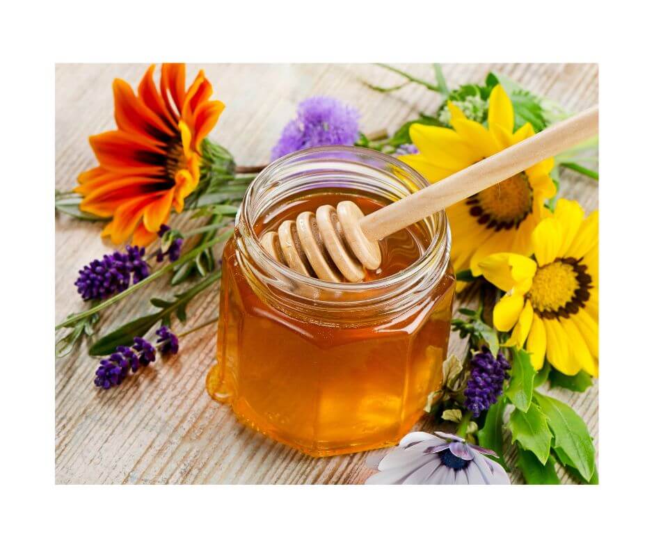 Ein Glas Honig angereichert mit ätherischem Lavendelöl bio und Blumen auf einem Tisch.