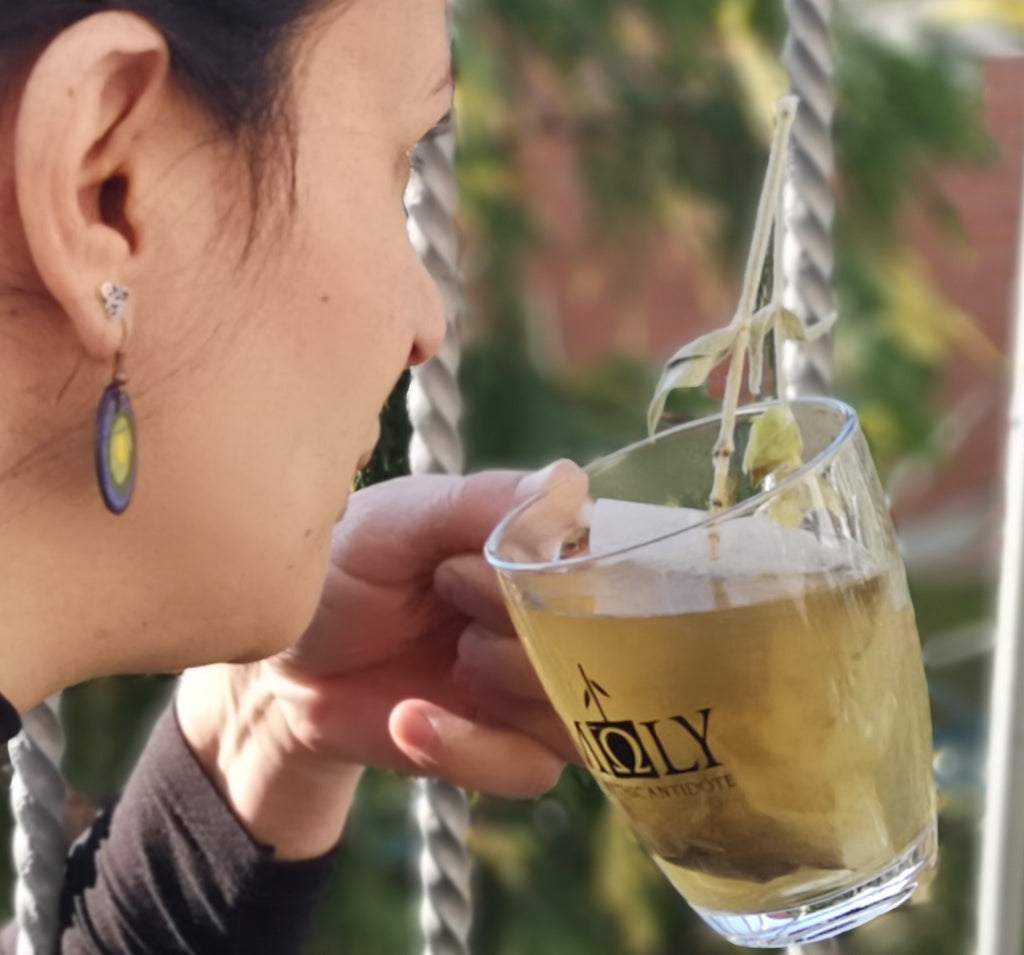 Eine Frau hält ein Glas mit Moly Tee und ist im Begriff einen Schluck Tee zu trinken.