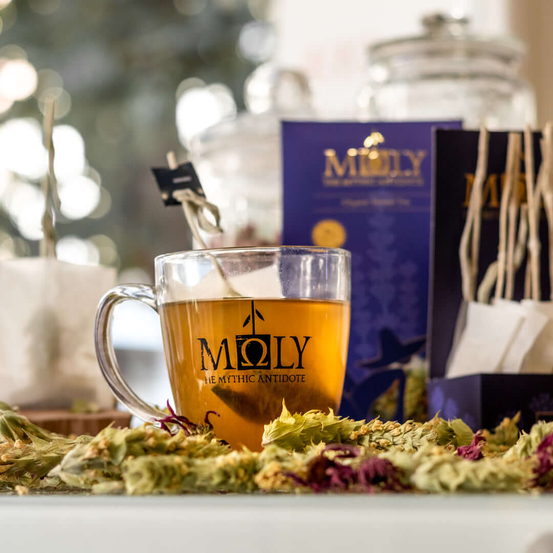 Eine Tasse mit Tee, Bergteeblüten liegen davor. Im Hintergrund die lila Verpackung des MOLY Night Cup