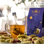 MOLY Night Cup BIO mit Stiehl im Glas und die lila Verpackung an der Seite. Bergteeblüten davor.