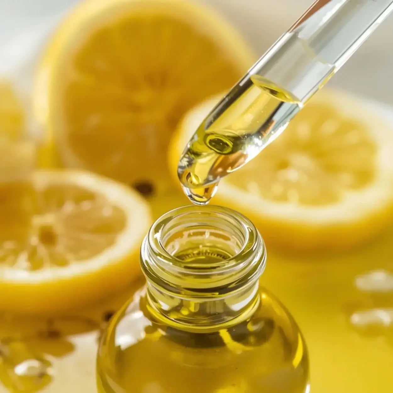 Zitronenscheiben und ein Glas Olivenöl. Eine Pipette träufelt Zitronenöl bio in das Glas.