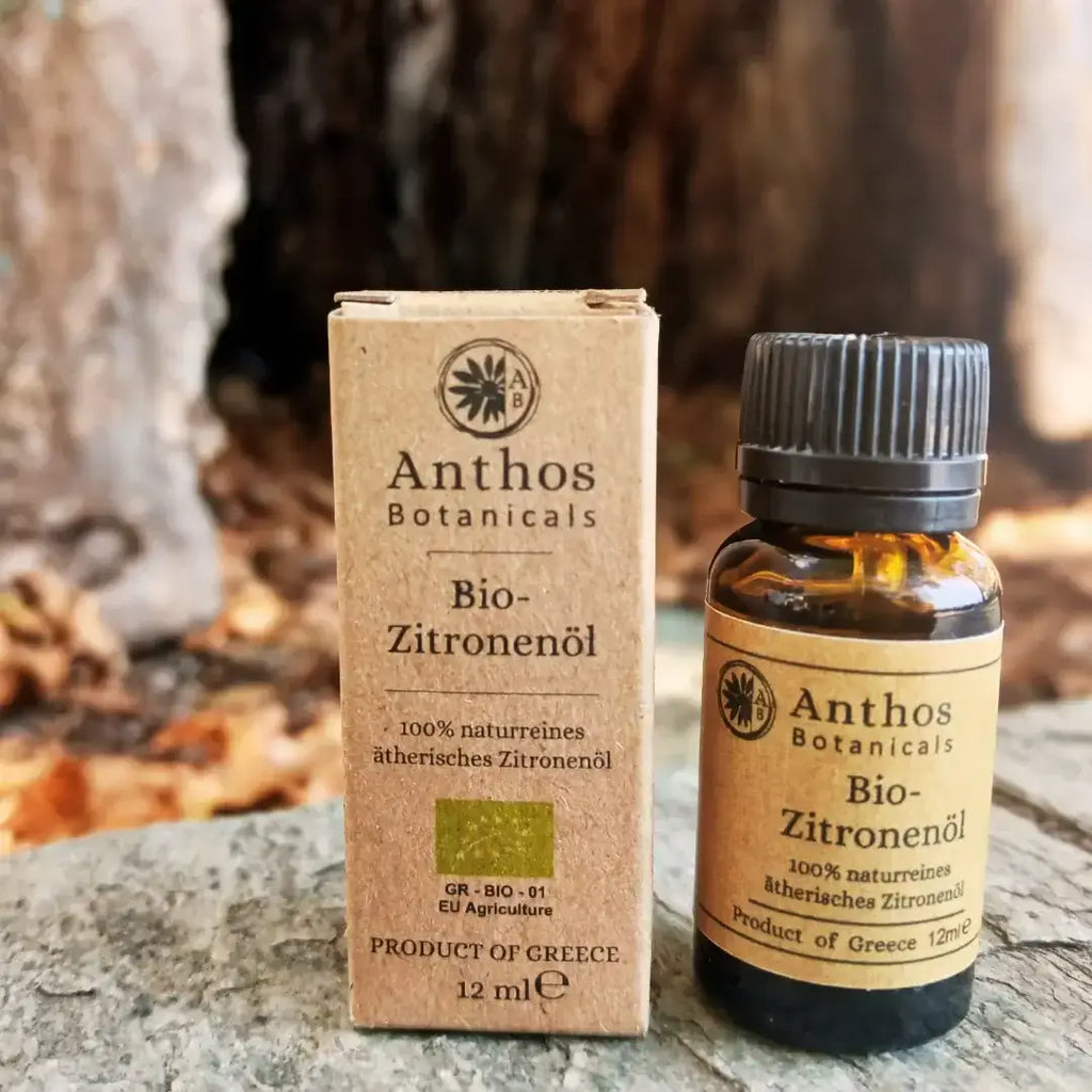 Braunglasflasche und Kraftverpackung mit biologischem Zitronenöl von Anthos Botanicals auf einem Felsen vor einem alten Baum.